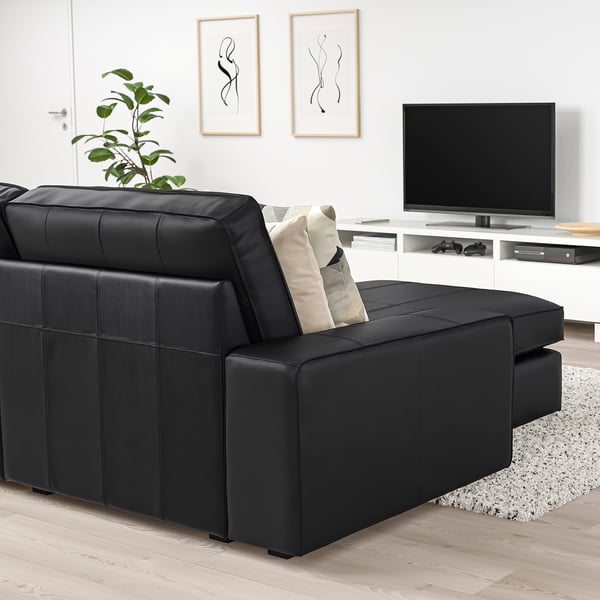 Moderno sofá KIVIK de cuero negro, con tumbona, cojines y mueble de tv, que ofrece un confort relajado en una amplia sala de estar.