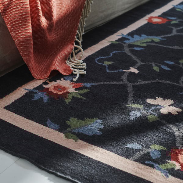 Alfombra de lana tejida a mano de color gris oscuro con diseños florales rosas y rojos, parcialmente cubierta por tela color coral.