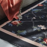 Alfombra de lana tejida a mano de color gris oscuro con diseños florales rosas y rojos, parcialmente cubierta por tela color coral.