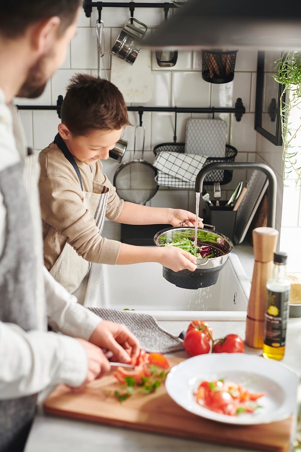 Dos personas cocinando en la cocina, una con colador KLOCKREN, la otra picando tomates.