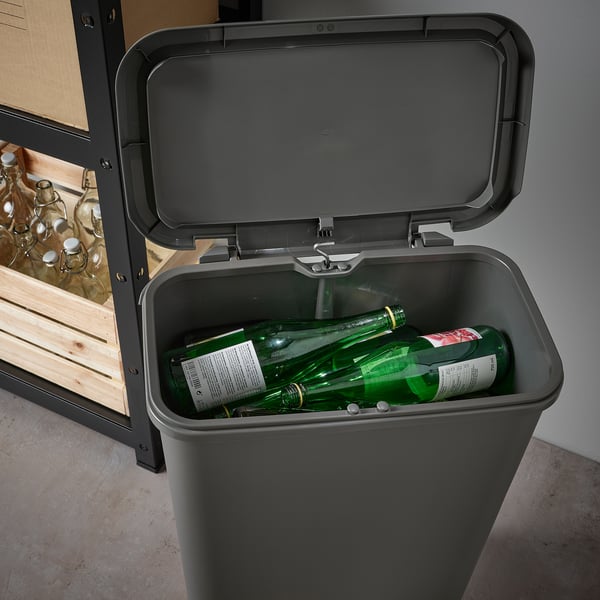 Un cubo de plástico negro con tapa abierta, que revela dos botellas verdes en su interior. La tapa tiene una bisagra de cierre suave.