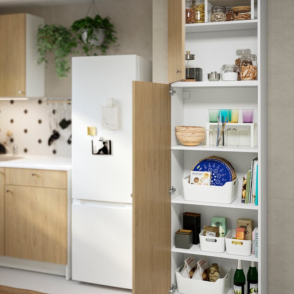 Armario de madera abierto que muestra artículos de cocina en una cocina moderna, con una nevera blanca cerca.