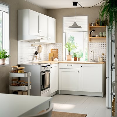 Moderna cocina blanca en forma de L con encimera de madera, electrodomésticos metálicos y amplio espacio de almacenaje. Ligero, aireado, con solución de esquina organizada.