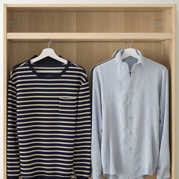 Armario de madera con dos camisas colgadas: una a rayas, otra azul claro. Se muestra con raíl KOMPLEMENT.