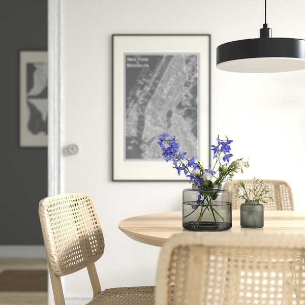 Comedor moderno con una mesa redonda de madera, sillas de mimbre claro, flores azules en un pequeño jarrón de vidrio transparente y un gran mapa enmarcado en la pared.