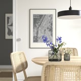 Comedor moderno con una mesa redonda de madera, sillas de mimbre claro, flores azules en un pequeño jarrón de vidrio transparente y un gran mapa enmarcado en la pared.