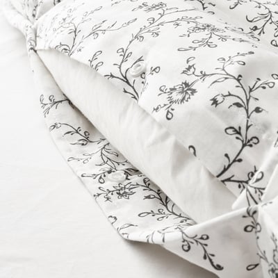 Edredón nórdico blanco con estampado floral negro, plegado con cierres a modo de botón a la vista.