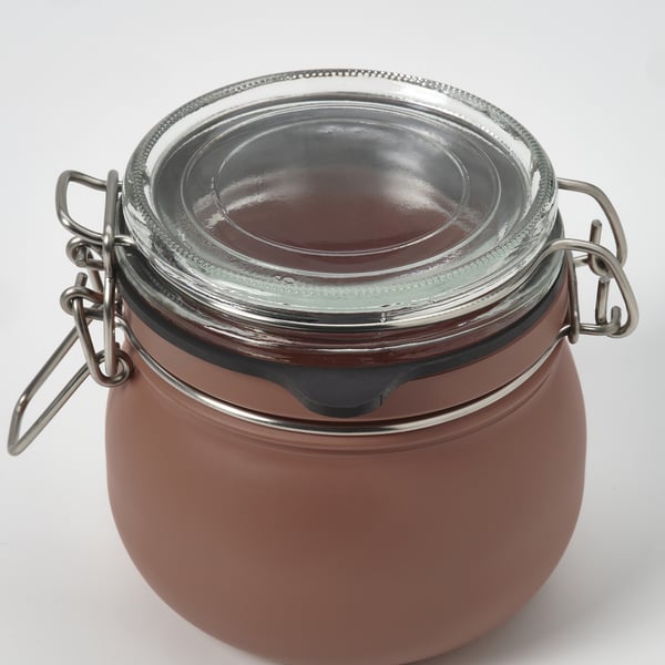 Tarro vacío y hermético con cierre metálico y tapa de cristal. Cuerpo redondo, de color marrón y superficie lisa. Sellado para conservar el contenido.