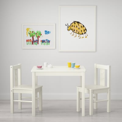 Área de juegos para niños con mesa y sillas blancas, tazas coloridas y arte con temas de insectos.