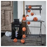 Las guirnaldas de luces KUSTFYR de Halloween, naranjas y blancas, junto a linternas y escobas, encajan bien en entornos festivos.