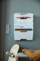 Organizador de archivos de pared KVISSLE blanco con carpetas de colores en la pared gris cerca de la patineta de madera.
