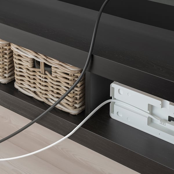 Las cestas de mimbre anidan dentro del banco de televisión oscuro LACK, los cables se manejan a través de la abertura trasera.