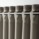 Primer plano de cortinas grises con cabeceras de bolsillo en forma de barra, mostrando su diseño para colgar a través de la barra de cortina.