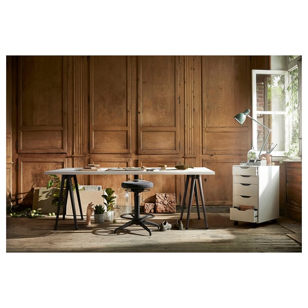 Configuración de la oficina en casa: escritorio blanco con taburete negro, plantas, lámpara en un armario blanco contra una pared con paneles de madera.