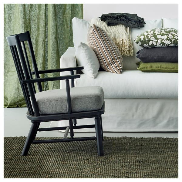 Una alfombra moderna de yute verde oscuro, silla negra y sofá blanco con almohadas verdes y neutras.