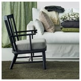 Una alfombra moderna de yute verde oscuro, silla negra y sofá blanco con almohadas verdes y neutras.