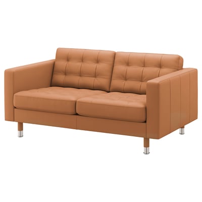 Un sofá de dos plazas de cuero marrón de IKEA. Tiene cojines capitoné y patas cromadas. Es un sofá elegante y cómodo.