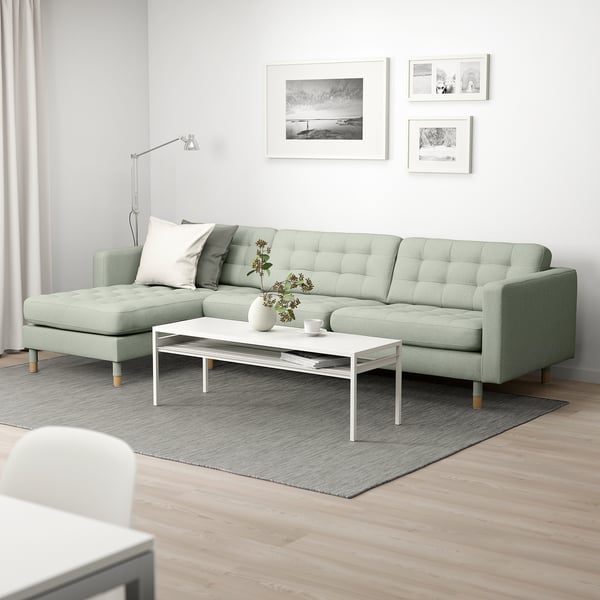Sala de estar moderna con sofá LANDSKRONA verde, tumbona, mesa de centro blanca, alfombra gris, arte de tres paredes, lámpara de pie.