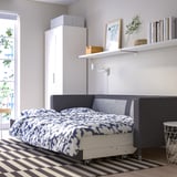 Dormitorio moderno con sofá cama convertible landskröna contra la pared, con tapicería gris con ropa de cama estampada, armario blanco y alfombra a rayas.