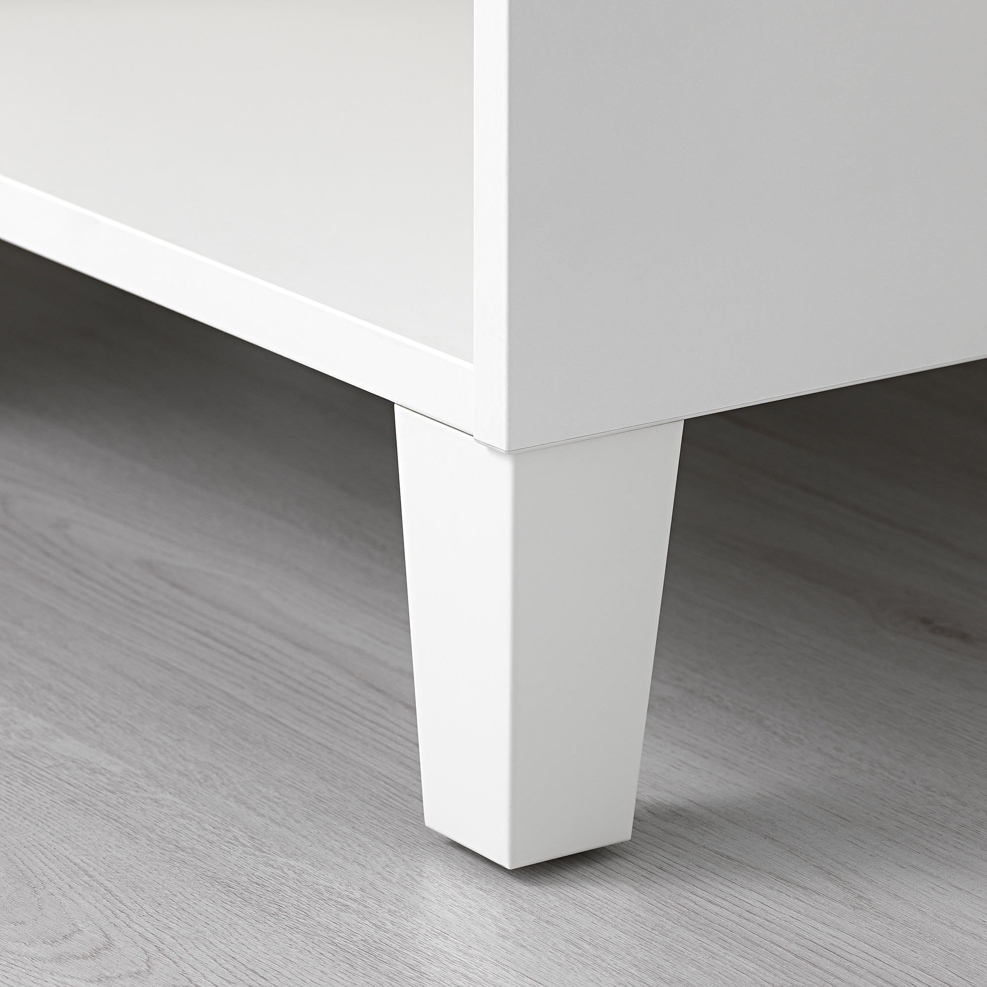 Primer plano de la pata de un mueble blanco con un diseño limpio y elegante, montado sobre suelo de madera, con un acabado de alta calidad.
