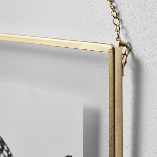 Cuadro colgante con marco dorado y líneas claras, unido a una cadena, contra una pared blanca, que muestra durabilidad y estilo.
