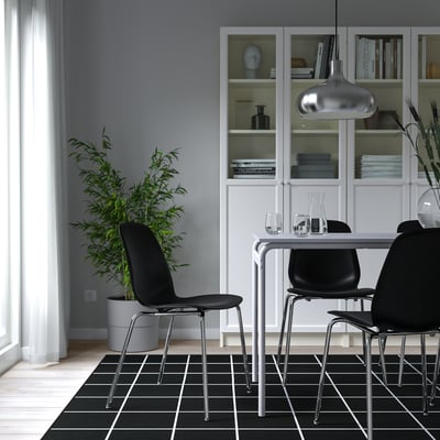Comedor moderno: elegantes sillas LIDÅS negras, patas cromadas, mesa de cristal, estantería blanca, elegante lámpara colgante. Alfombra oscura de cuadros.