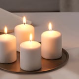 Cinco velas blancas encendidas en una bandeja redonda de metal, creando un cálido resplandor ambiental.