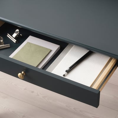 Cajón de escritorio abierto con cuadernos, lápiz y asa.
