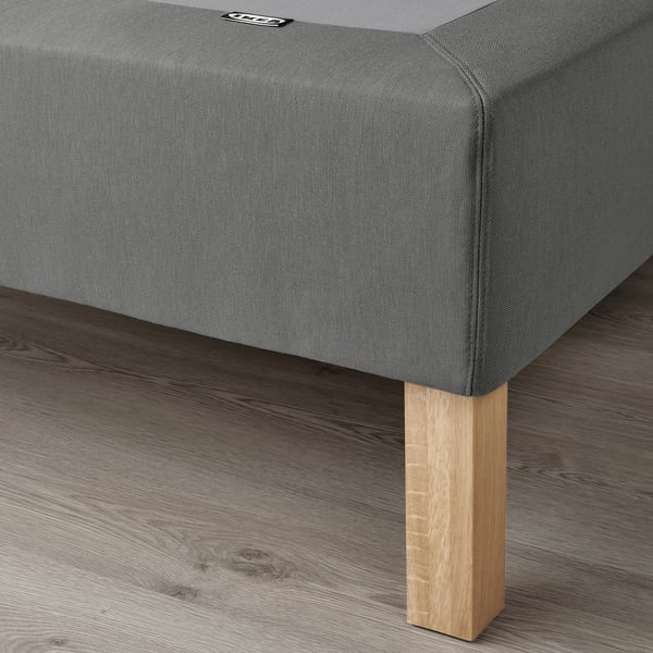 Un somier gris con patas de madera a la vista, que ofrece soporte y flujo de aire, colocado sobre un suelo de madera.