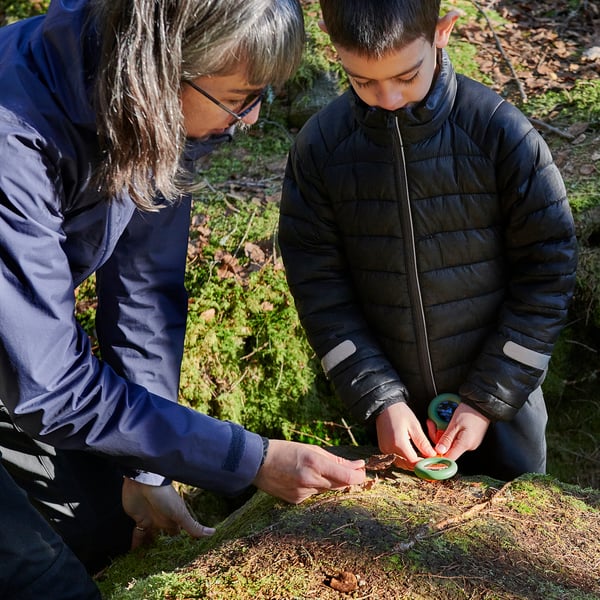 Dos personas examinan la naturaleza con lupa y brújula, aprendiendo al aire libre.