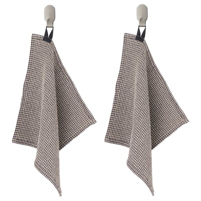 Dos paños de cocina de pata de gallo cuelgan de ganchos metálicos, lazos negros en la parte superior, patrón de cuadros beige y negro.