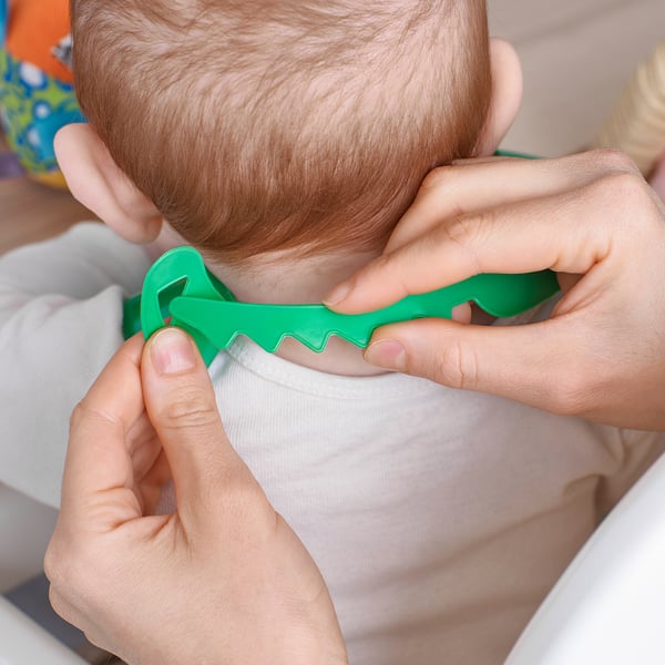 Las manos de los adultos alimentan a un bebé con una cuchara verde. El diseño de la cuchara ayuda a que las manos pequeñas lo sostengan fácilmente, como se muestra en el primer plano.