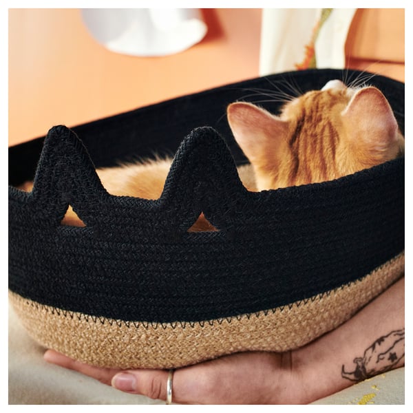 Un gato se asoma de una cesta de yute negro; Textura tejida, forma redonda con recortes triangulares.