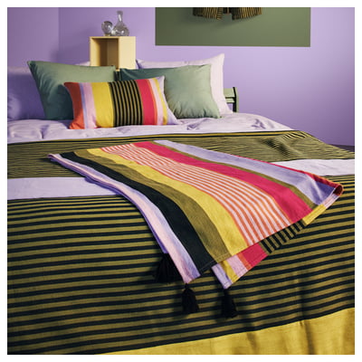 Manta de rayas MÄVINN en la cama, con rayas vibrantes, tejida a mano, borlas en los extremos.