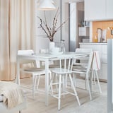 Comedor moderno con mesa y sillas MELLTORP blancas, diseño minimalista, suelo de madera, lámpara en el techo y cortina beige.
