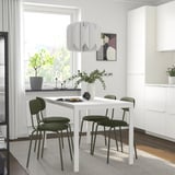 Mesa de comedor MELLTORP blanca con sillas, planta, lámpara y decoración de color verde oscuro.