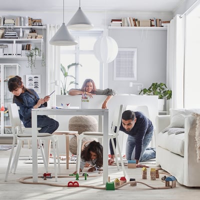 Familia disfrutando de la mesa MELLTORP blanca; Decoración minimalista con sillas blancas y grandes ventanales.