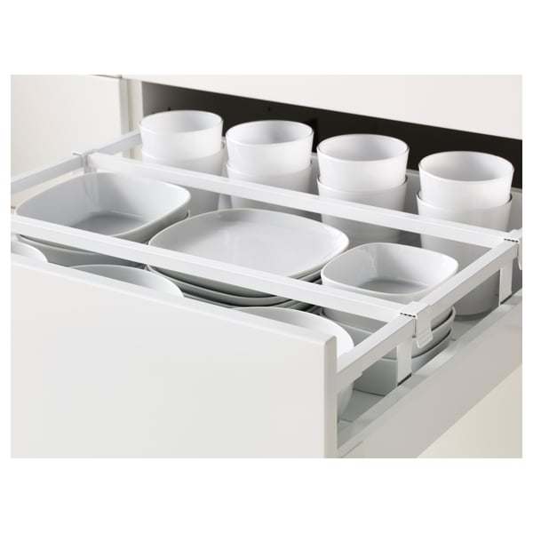 Organizador de cajones de cocina blanco con múltiples compartimentos que contienen tazones y tazas de cerámica blanca. Forma parte del sistema de cocina METOD.