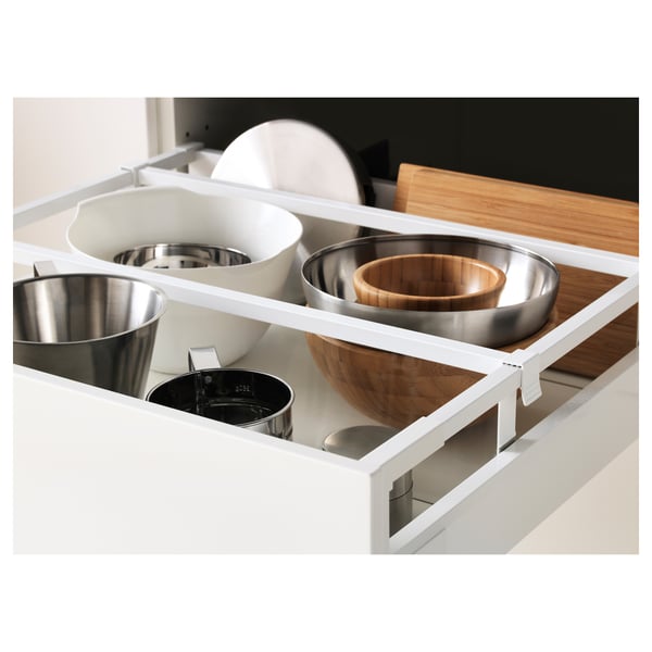 Organizador de cajones de cocina blanco con ollas de acero inoxidable, cuencos de madera y una tabla de cortar.