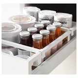 Cajón de cocina blanco con varios frascos y recipientes de vidrio transparentes y etiquetados.