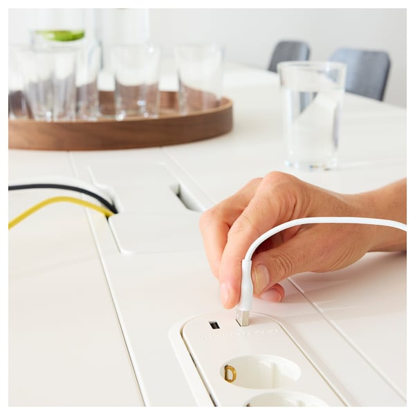 La mano conecta el cable MITTZON blanco en la toma de corriente modular en la mesa de conferencias blanca.