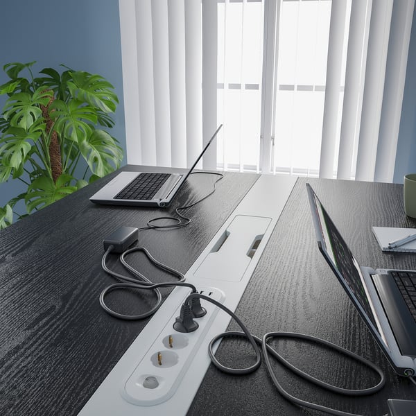 Moderna mesa de conferencias alta con tomas de corriente integradas y gestión de cables para sentarse o estar de pie. Una planta en maceta agrega vegetación al lado de las ventanas.