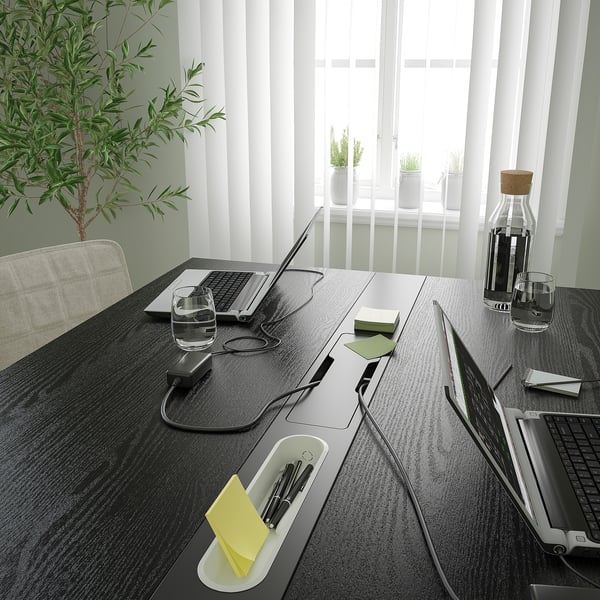 Moderna mesa de oficina oscura con estaciones de carga, agua y computadoras portátiles.