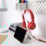 Pequeños auriculares rojos se colocan en el escritorio con la tableta, junto a los libros y la lámpara. Acero recubierto de epoxi, en forma de V, encaja perfectamente entre los artículos.