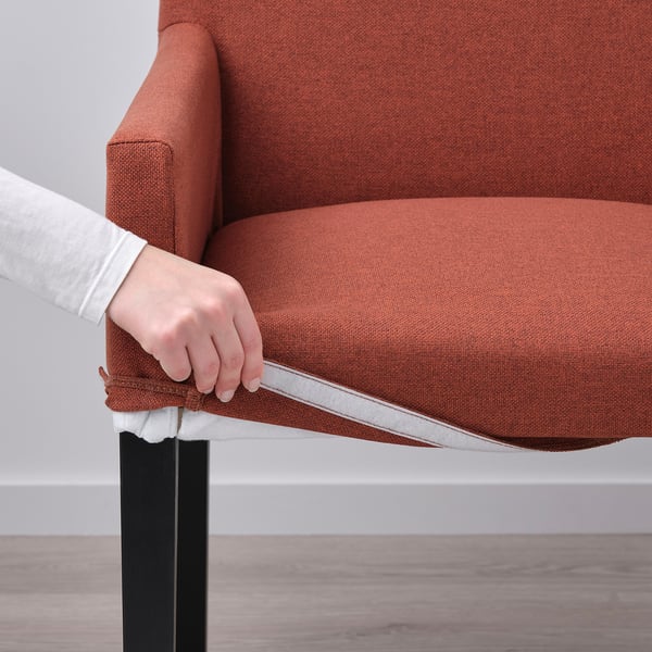 Una mano ajustando una funda extraíble en una silla MÖRBYLÅNGA naranja.