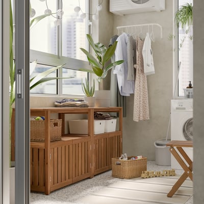 Lavadero moderno con almacenamiento de madera NÄMMARÖ, lavadora blanca, perchero, plantas y juguetes.