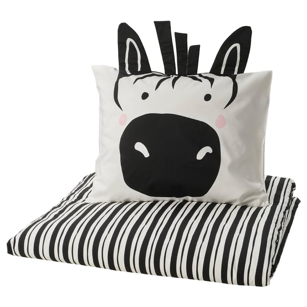 Almohada en blanco y negro con temática de cebra sobre manta a rayas.