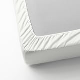 Un primer plano de una sábana blanca de ensueño, suave como la seda, con un brillo sutil y bordes elásticos, diseñada para colchones de hasta 26 cm de grosor.