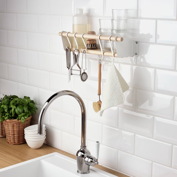 Configuración organizada de la cocina. Los estantes cromados para grifos, plantas y colgantes almacenan platos y utensilios en un protector contra salpicaduras blanco.