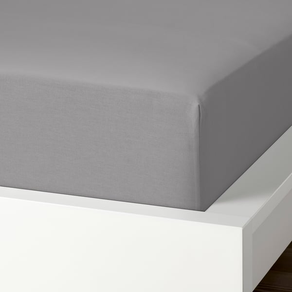 Una sábana bajera de algodón gris desplegada sobre una estructura de cama blanca, que muestra su textura suave y transpirable y su borde elástico.